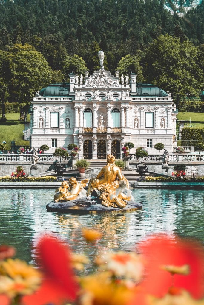 gold fountain in lake outside white stone palace and gardens at Linderhof Palace