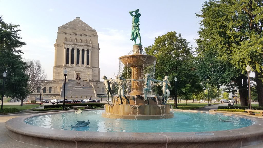 white stone Indianapolis War Memorial and nearby fountain with aqua blue water and water nymph statues