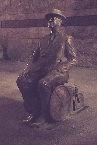 Metal statue of Franklin Delano Roosevelt seated in wheelchair as seen at night