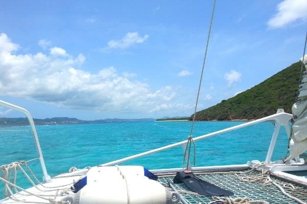 White catamaran rigging in front of aqua blue ocean, blue skies, and green Buck Island, St Croix, USVI