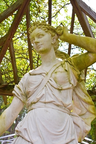 white stone statue of the goddess Diana surrounded by a wooden arbor covered in green leaves