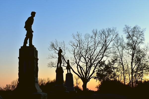 Battlefield Memorials at Antietam National Battlefield are black against the sun setting behind the trees