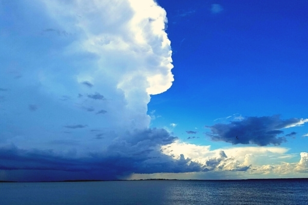 Tall and dark storm clouds soar over the ocean from the right contrasting with the bright blue sky on the left