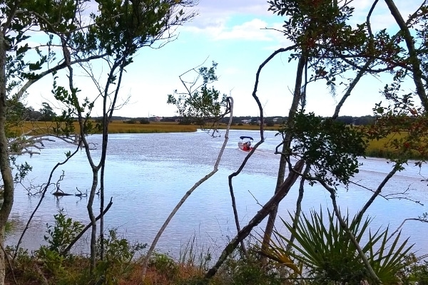A boat glides along Scott Creek in Edisto Beach State Park surrounded by yellow-brown marsh and a blue sky overhead