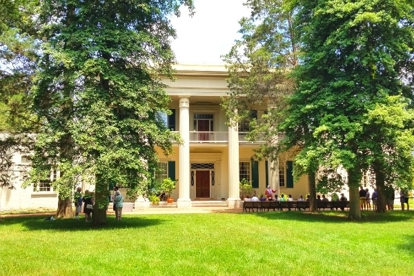 Celebrate Presidents' Day at the The Hermitage, Andrew Jackson's home in Nashville, TN, featuring columned front facade with large green front lawn and large trees out front.