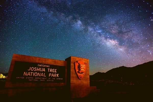 Starry deep blue milky way sky with a Joshua Tree National Park sign in the foreground