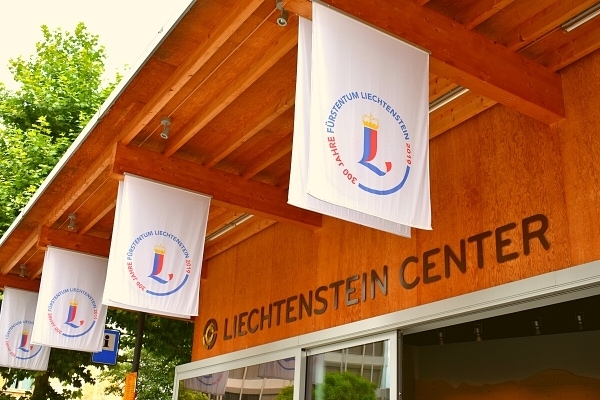 White banners with Liechtenstein logos hang from the wooden beams of the Liechtenstein Center's roof on a sunny day