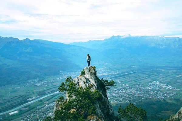 A lone hiker stands atop a rocky outcropping in the mountains above the Rhine River and Liechtenstein