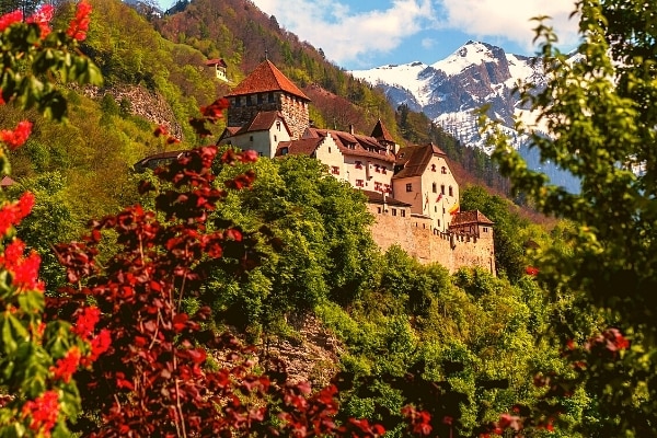 Vaduz Castle sits on a hill above the city, surrounded by lush vegetation and with snowy mountains in the background