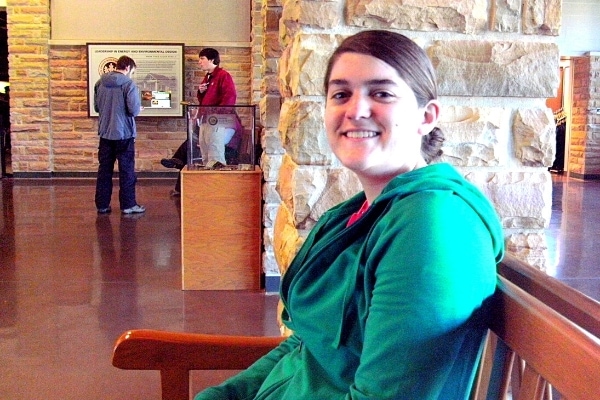 A woman in a green jacket smiles from a brown bench in the lobby of the Mammoth Cave National Park Visitor Center