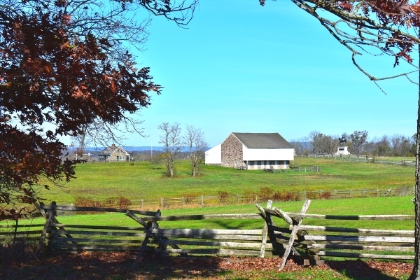 White and brown McPherson Barn surrounded by green fields, wooden fences, and a blue sky at Gettysburg Battlefield