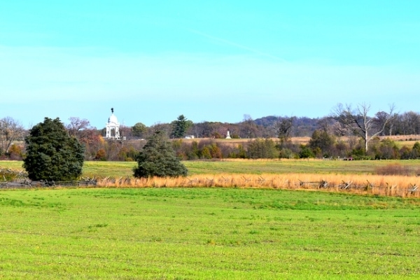 Green field and tall yellow grass surround Plum Run At Gettysburg Battlefield with the white stone Pennsylvania Memorial in the distance