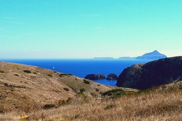 Yellow grassy hills of Santa Cruz island look out across the blue Santa Barbara Channel at Anacapa Island in the distance