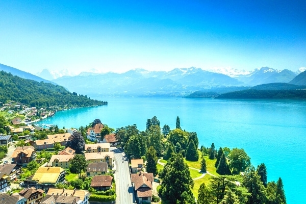 Small Swiss town on the shore of an aqua blue lake with snow capped mountains in the distance