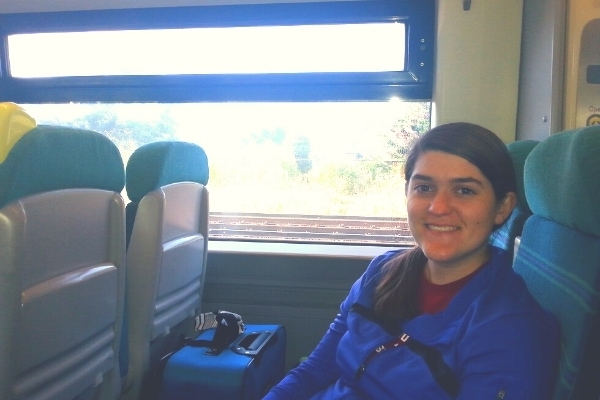 A woman in a blue jacket smiles from her seat on the train