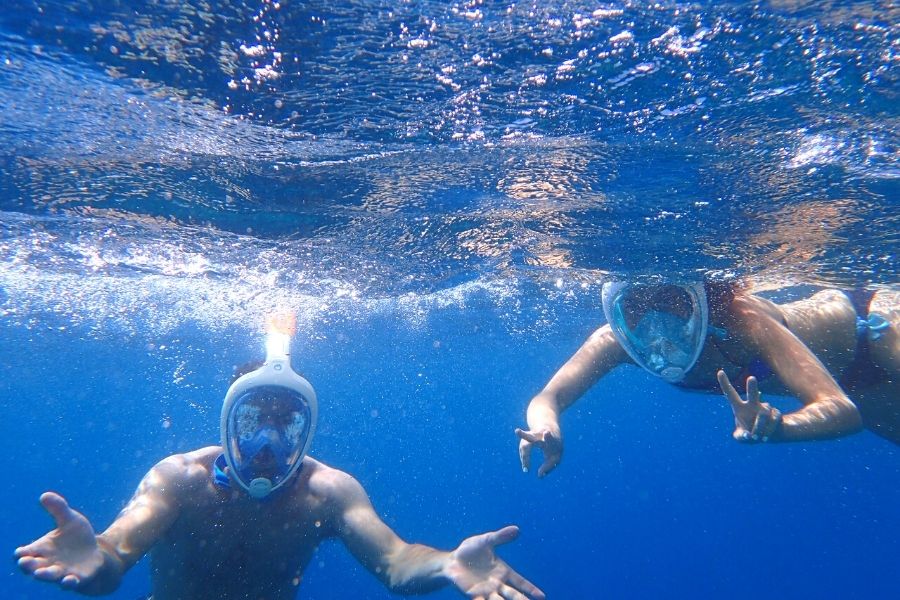 Two snorkelers using full-face snorkel mask in blue water