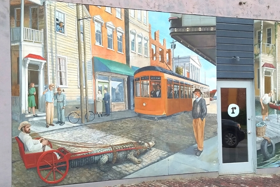 Colorful and whimsical mural on the side of a building showing a cable car and a gator pulled rickshaw