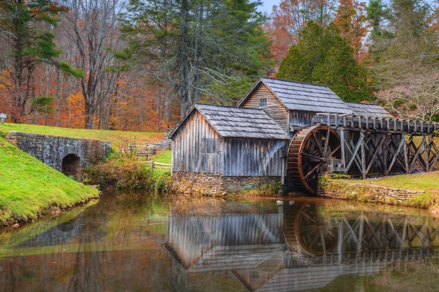 The old wooden Mabry Mill with waterwheel sits on the edge of a pond surrounded by a forest in fall