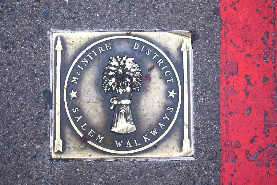 Metal plaque set in asphalt denoting the McIntire Historic District with and arrow and red stripe pointing the way for the walkway