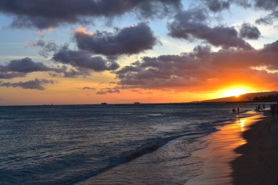 Vibrant orange sunset behind a mountain ridge, reflected across the beach in Oahu