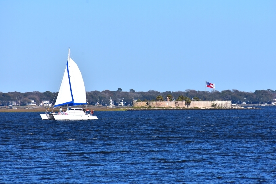 A white sailboat floats on a deep blue Charleston Harbor in front of Castle Pinckney