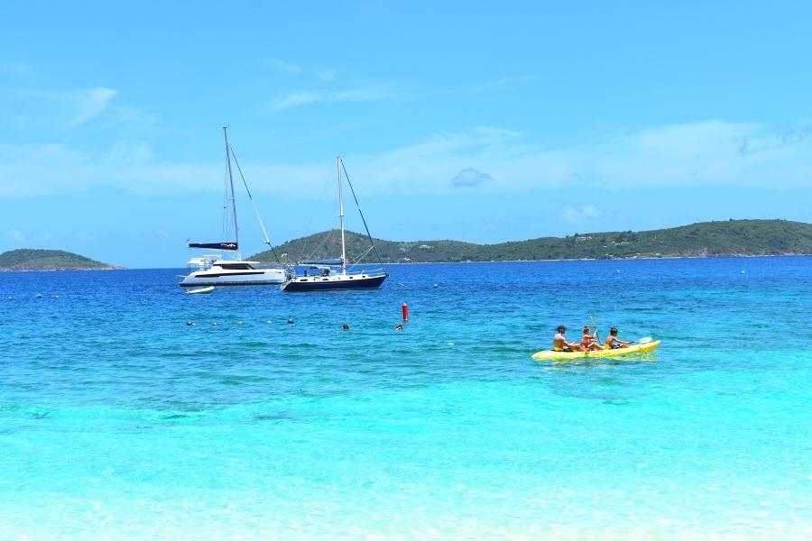 Aqua blue waters of Honeymoon Bay Beach with two sailboats and a family in a yellow kayak in St John, USVI