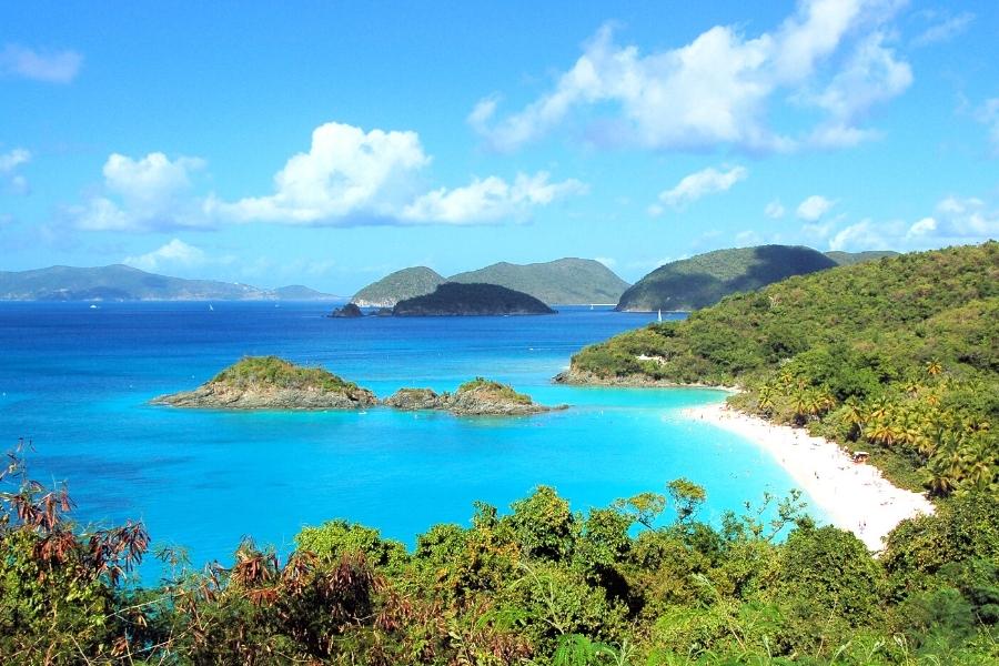 Blue aqua bay with a white sand beach and a rocky cay in Trunk Bay, St John