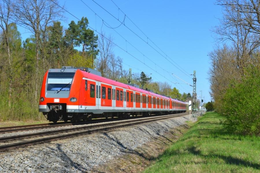 A red electric train rolls down the tracks in a green outdoor setting