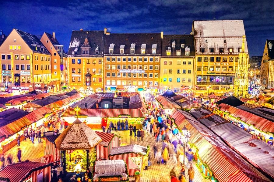 Nuremberg's Hauptmarkt square covered with Christmas market stalls, aglow at night with crowds of people