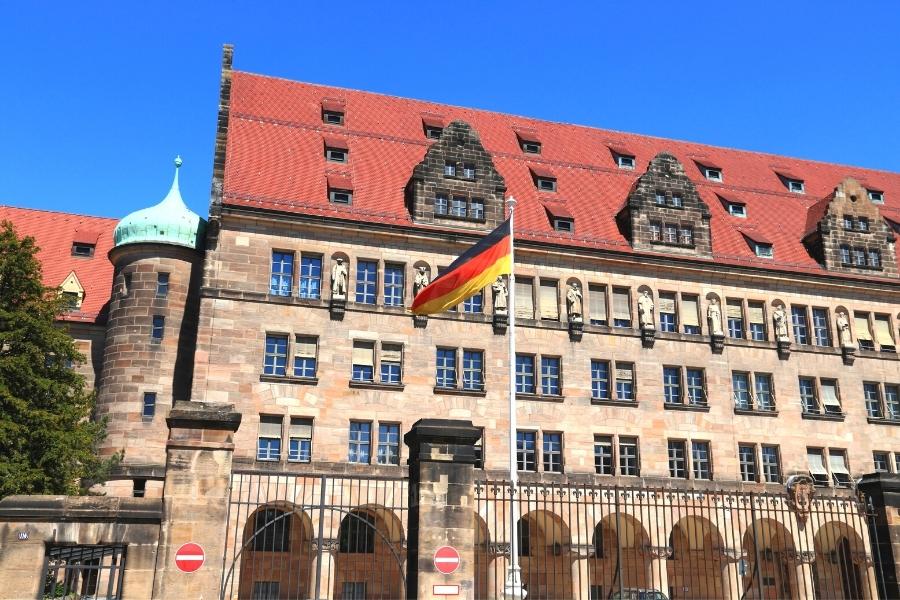 Nuremberg's Palace of Justice tan stone building with red tile roof, statues along the roofline and a German flag waving in the foreground