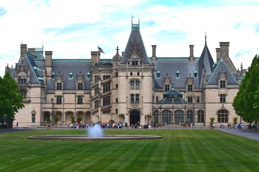 Lines queue in front of the enormous French chateau-inspired Biltmore House with a small fountain in the middle of the green lawn in the foreground