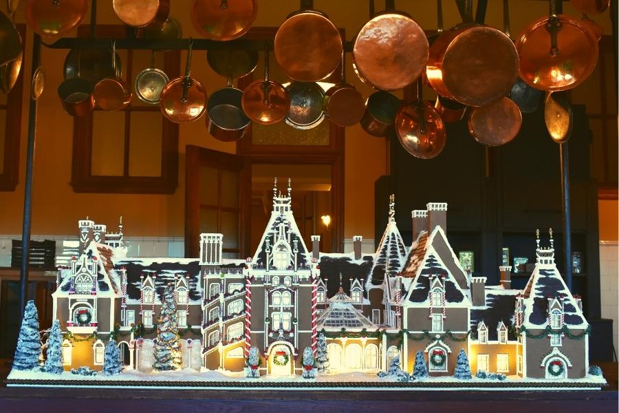 Copper pots hang on a rack above the main table in the Biltmore kitchen which holds an intricately designed gingerbread house replica of the Biltmore Mansion