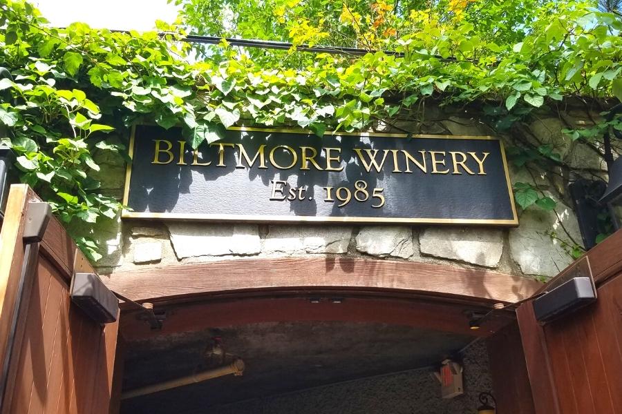 Metal sign for "Biltmore Winery, Est. 1985" above the entrance to the Biltmore Estate Winery, surrounded by green ivy