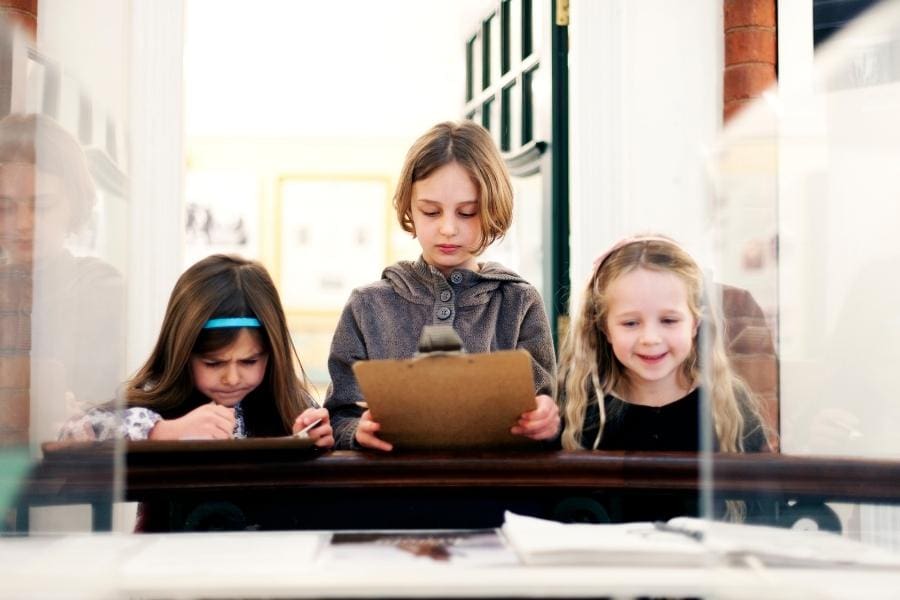 Three young girls interact with a museum exhibit in a brightly lit exhibit hall