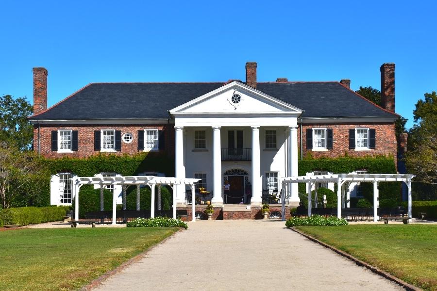 Two story brick Boone Hall House with white pillar colonnade over the front porch and white arbors on either side of the front steps
