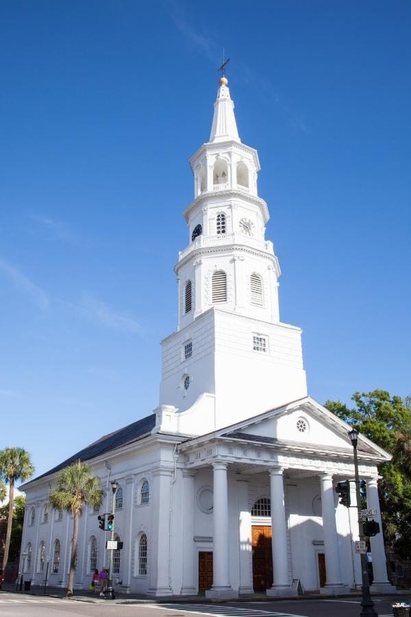 St Michael's Church in Charleston, SC towers over palmetto trees, glistening pure white against a blue sky