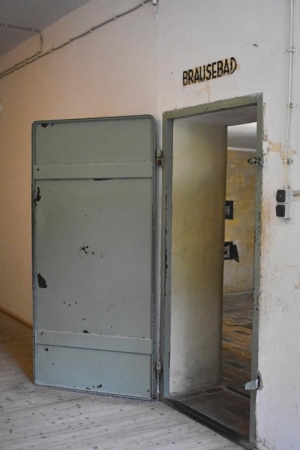 An old gray metal door sits open with the word Brausebad on the wall above it, the entrance to the gas chamber at Dachau Concentration Camp
