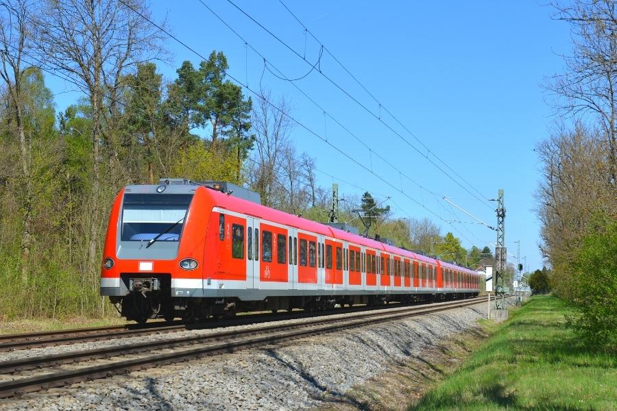 A red and gray train on tracks passing through a green countryside under a blue sky