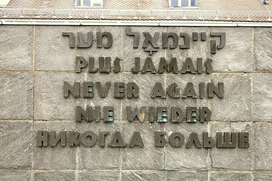 A list of metal words in 5 different languages on a stone wall at the Dachau Concentration Camp Memorial Site, each the same phrase: Never Again