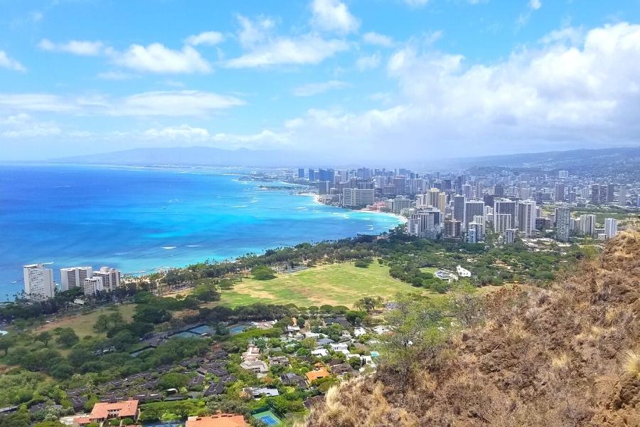 View from atop Diamond Head Crater, looking out across green Kapiolani park and the blue ocean to the skyscrapers of Honolulu
