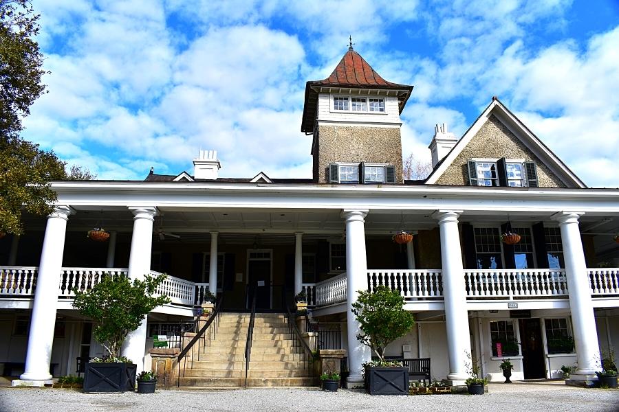 Large multi-story Magnolia Plantation house with a copper roof turret and gray stucco under a cloudy blue sky