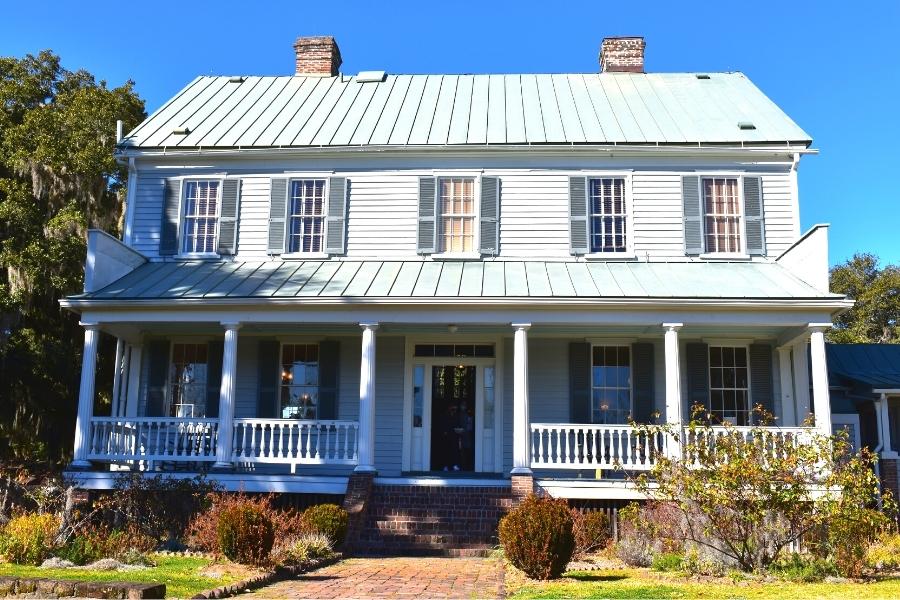 Two story plantation home with a green metal roof and covered porch with rocking chairs