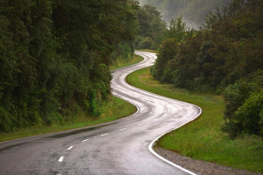 A paved road winds its way through a dark green forest in the mountains