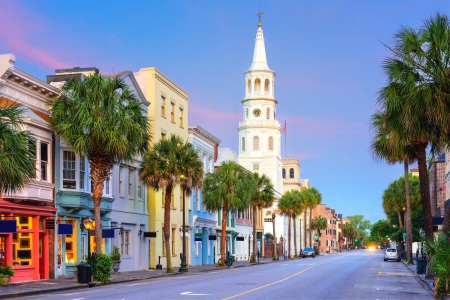 Colorful buildings and church on Broad Street in Charleston, SC glows as the sun sets and the sky turns purple