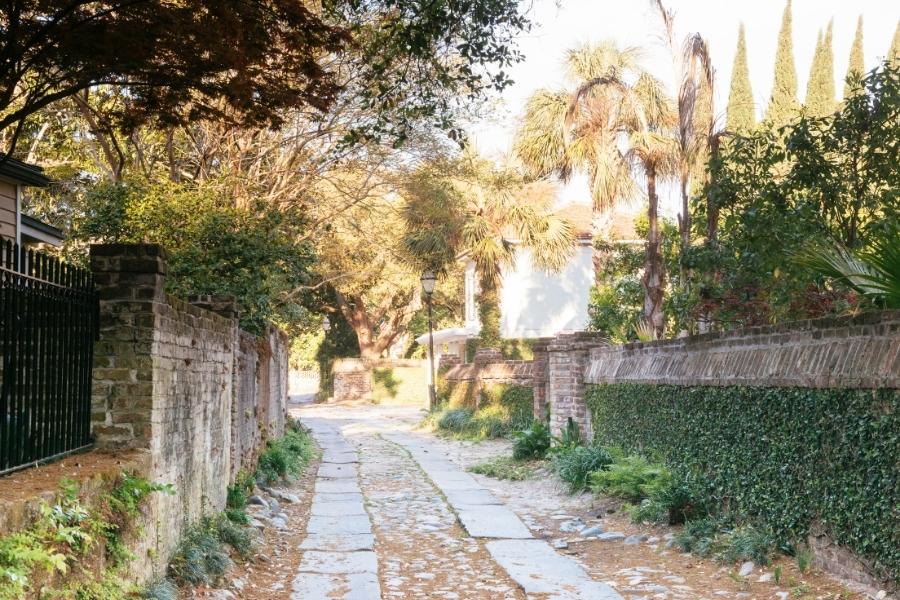 Longitude Lane in Charleston, SC is a cobblestone lane between historic houses delineated by brick walls and overflowing with greenery