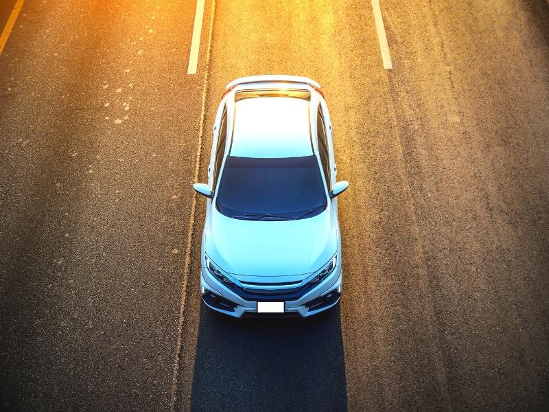 White car on a black roadway with the glow of a sunset behind it