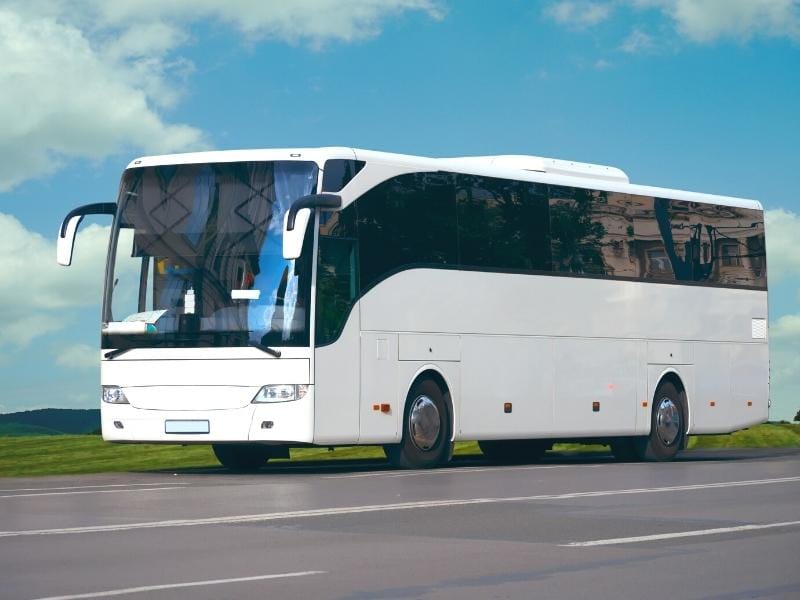 White tour bus on a roadway under a blue sky