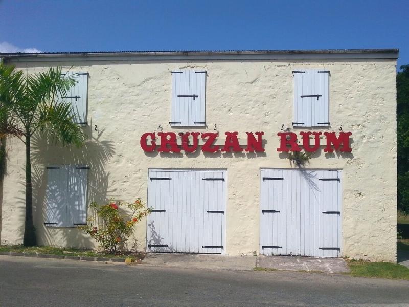 A cream two-story building with white shutters and a bold red sign for Cruzan Rum at the Cruzan distillery in St Croix
