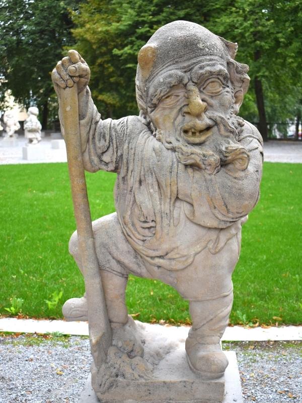 A small statue of a dwarf with an old man's face and beard and a bump on his head, leaning on a walking stick