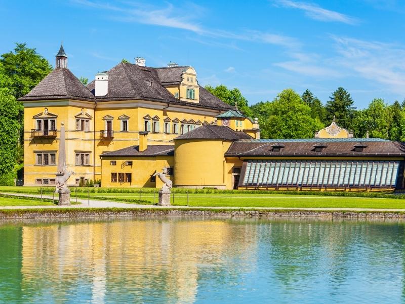 Yellow stucco Hellbrunn Palace in Salzburg, Austria is reflected in a pond outside the palace entrance